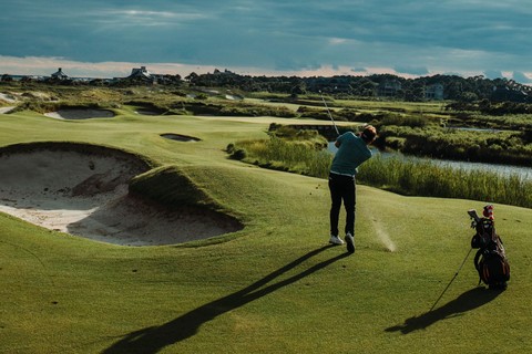 A man having just taken a golf shot over a sand bunker